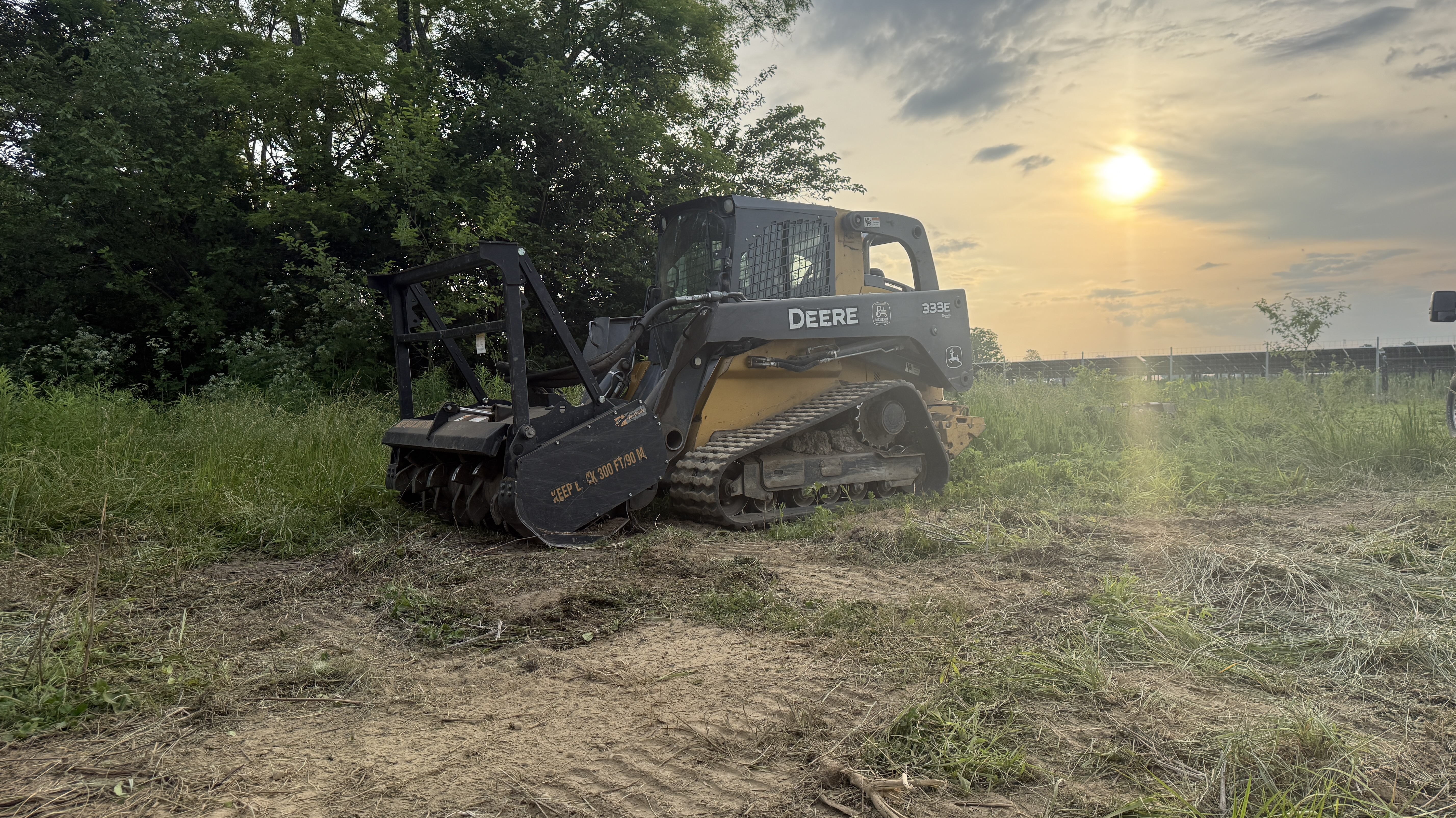 John Deere skid steer with forestry mulcher attachment at sunset